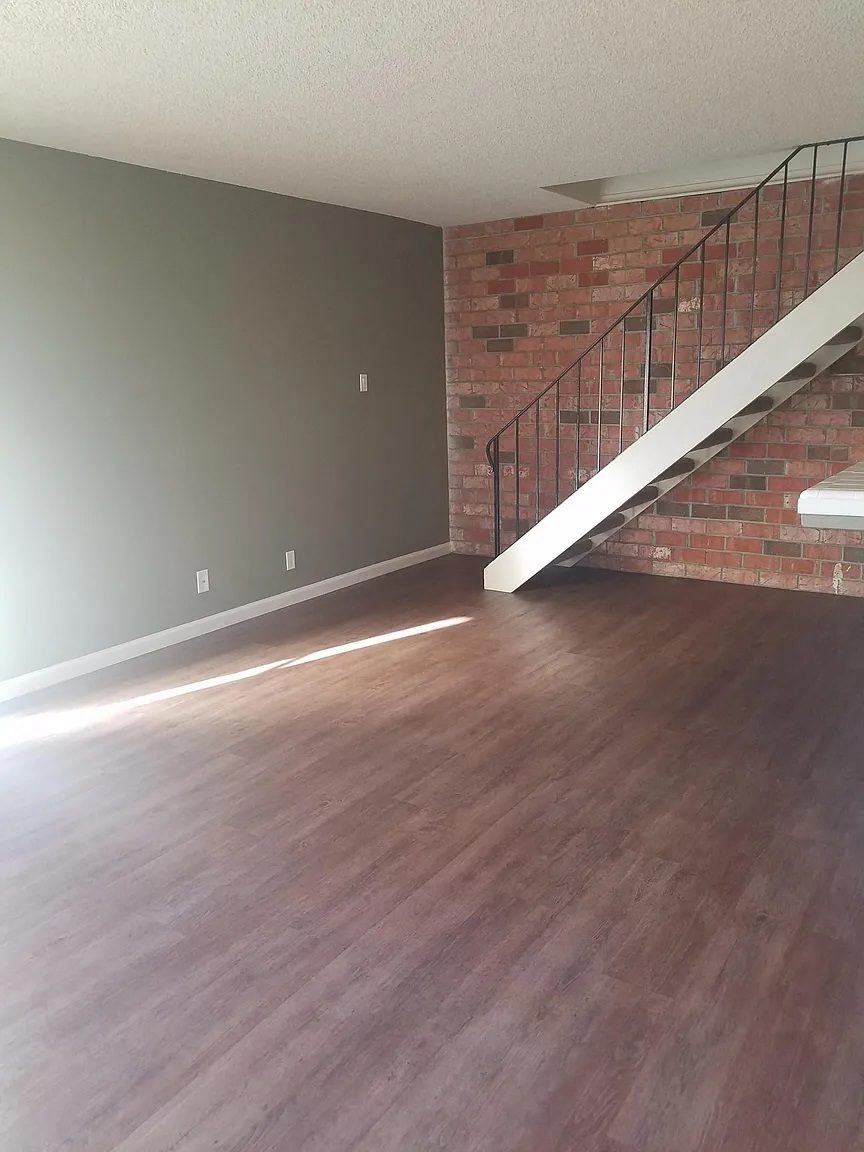 A room with a wooden floor and a staircase with a metal railing.